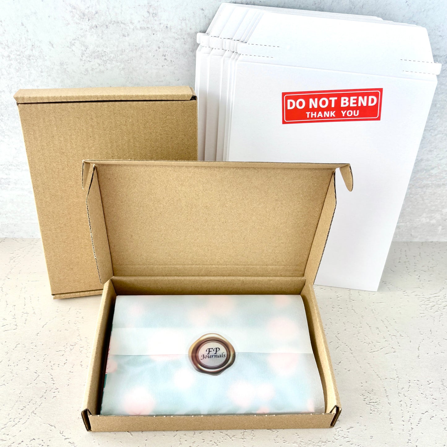 Packaging for A5 Blank Travelers Notebook Insert – Fountain Pen Friendly, Hand-Stitched Kraft Cover showing a sealed wrapped insert inside an open kraft cardboard box with mailing envelopes in the background.
