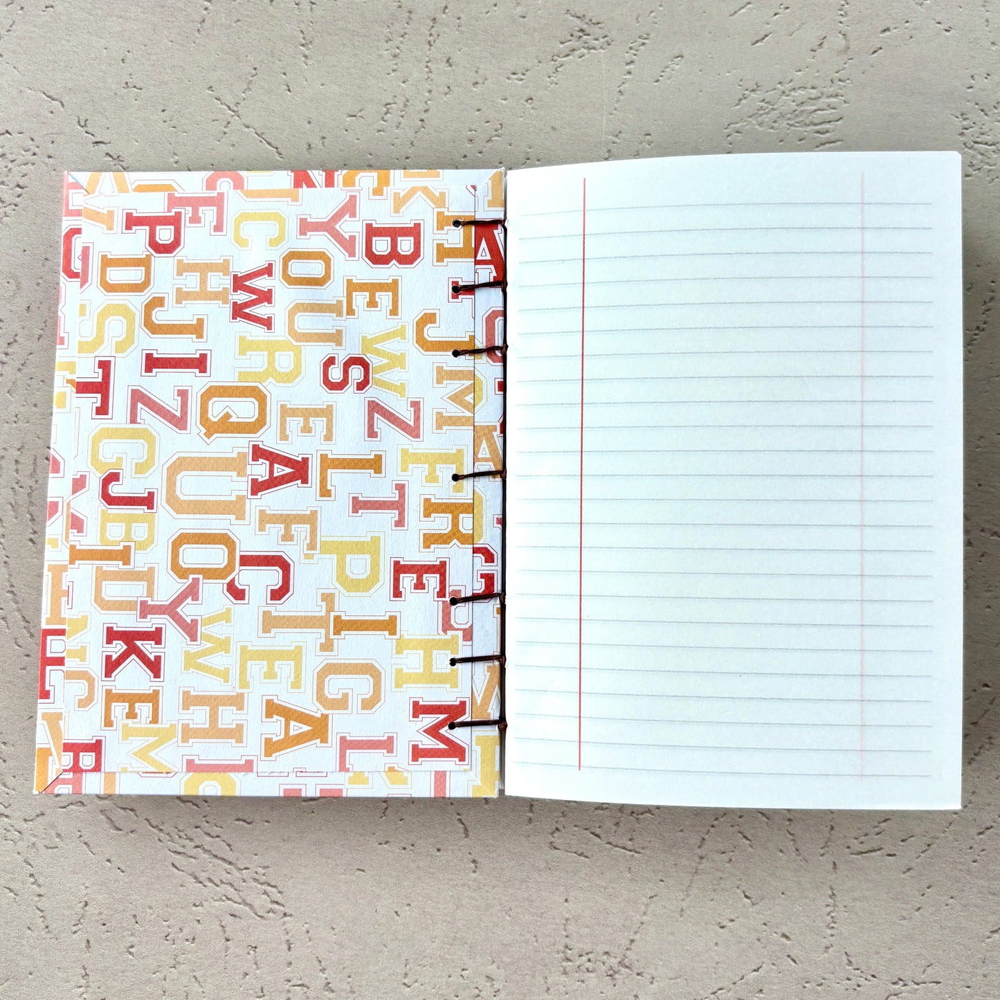 University Monogram - A6 - Lined - Coptic Bound - Fountain Pen Notebook - Handmade Journal open to lined pages with colorful monogram cover and stitched binding