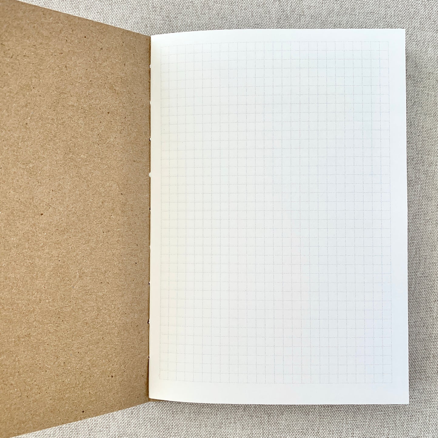 Open A6 Graph Travelers Notebook Insert - Fountain Pen Friendly, Hand-Stitched Kraft Cover showing clean graph grid pages and natural kraft stitched binding on a neutral fabric background.