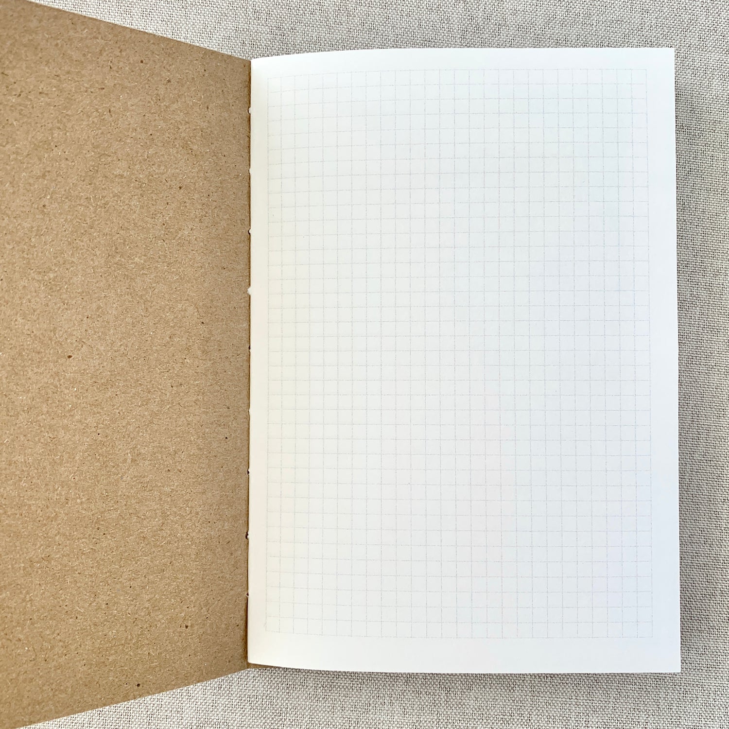 Open A6 Graph Travelers Notebook Insert - Fountain Pen Friendly, Hand-Stitched Kraft Cover showing clean graph grid pages and natural kraft stitched binding on a neutral fabric background.